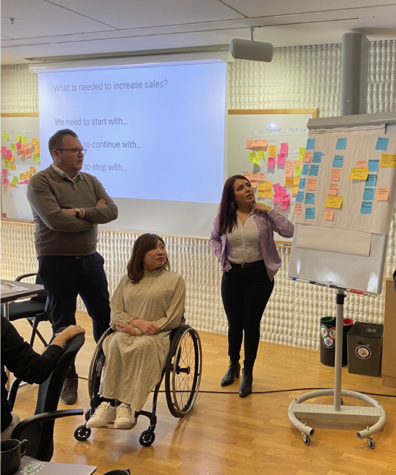 Consuelo leading a workshop with colleagues in front of a board of sticky notes